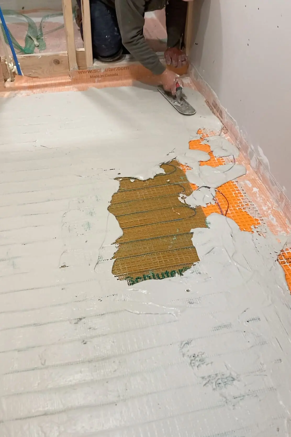 A worker carefully applying thinset mortar over a Schluter-DITRA underlayment in a bathroom renovation project, ensuring an even spread and proper adhesion for tile installation.